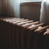 Ряд старых батарей отопления у окна за полупрозрачными шторами