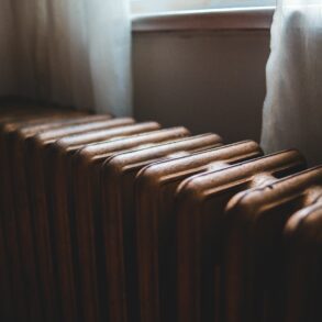 Ряд старых батарей отопления у окна за полупрозрачными шторами