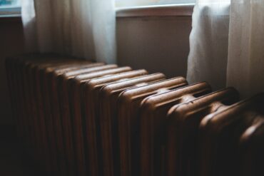 Ряд старых батарей отопления у окна за полупрозрачными шторами