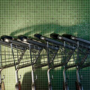 Несколько пустых металлических магазинных тележек у зеленой плиточной стены