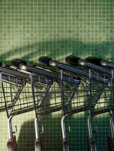 Несколько пустых металлических магазинных тележек у зеленой плиточной стены