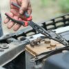Рука с пассатижами работает возле аккумулятора автомобиля под открытым капотом